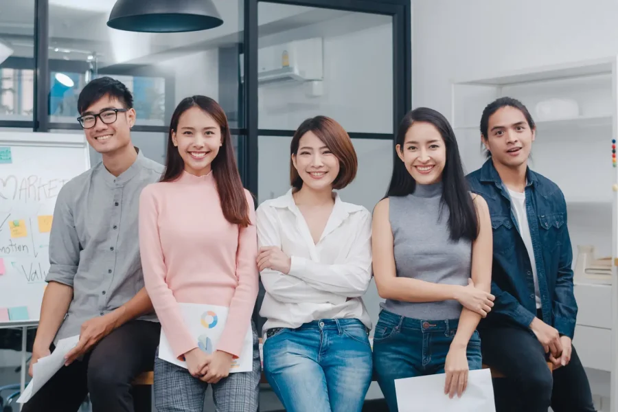 Group of Asia young creative people in smart casual wear looking at camera and smiling in creative office workplace. Diverse Asian male and female stand together at startup. Coworker teamwork concept.